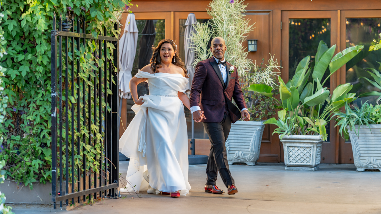 Bride and groom walking hand in hand through a garden gate